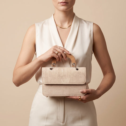 Tasche aus weißem Kork mit Griff aus Naturkork, die ein leichtes und ausgewogenes Erscheinungsbild schafft. Die Klappe mit Magnetverschluss und die offene Vordertasche ermöglichen schnellen Zugriff. 